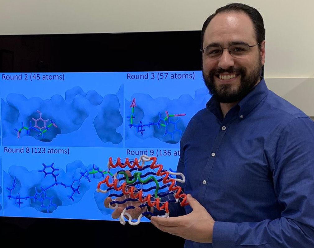 Dinler holding a 3D model of the binding site of a peptide-MHC complex. In the back, the incremental docking of a peptide to an MHC.